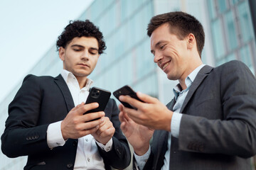 Male brokers hold phones in their hands. Economists are discussing further actions on the project. Businesslike young people.