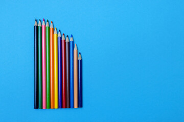 Colored wooden pencils on a blue paper background. Vertically upwards, place for text about school or drawing lessons.