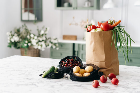 Various vegetables in paper grocery and black mesh bags on kitchen island