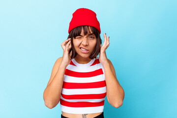 Young mixed race woman isolated on blue background covering ears with fingers, stressed and desperate by a loudly ambient.