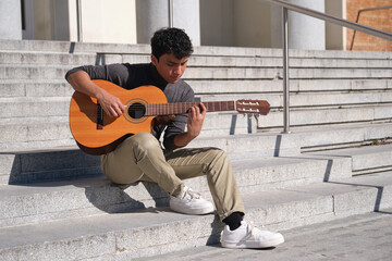 Latin young man playing guitar sitting on stairs. Playing guitar outdoors.