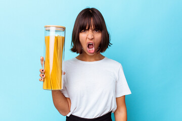 Young mixed race woman holding pasta jar isolated on blue background screaming very angry and aggressive.