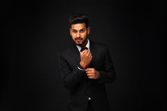 Portrait of young stylish indian business man in black suit on black isolated background