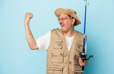 Senior indian fisherman holding rod isolated on blue background raising fist after a victory, winner concept.
