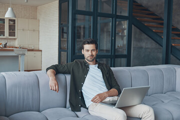 Handsome young man using laptop while sitting on the sofa at home