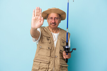 Senior indian fisherman holding rod isolated on blue background standing with outstretched hand showing stop sign, preventing you.