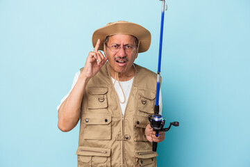 Senior indian fisherman holding rod isolated on blue background showing a disappointment gesture with forefinger.