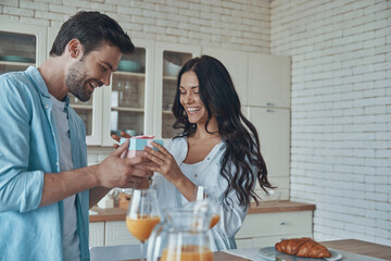 young man giving a gift box to his girlfriend while having breakfast at the domestic kitchen