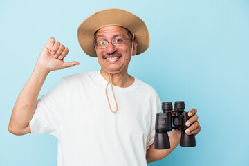 Middle aged indian fisherman holding rod isolated on blue background feels proud and self...