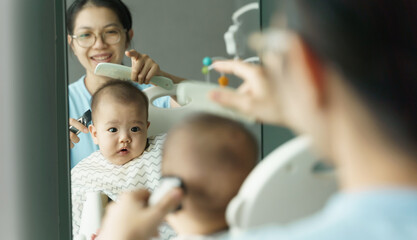 Happy Smiling Asian Young Mother cutting hair to her little baby son by herself at home
