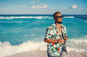 Handsome happy man wearing hawaiian shirt at the sea or the ocean background. Travel vacation holiday. Man walking at the sea, enjoy tropical season - obrazy, fototapety, plakaty