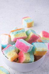 marshmallows, colorful soft sugar confection in a bowl, closeup view of cube shaped candy scattered on a white background