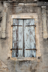 Ein alter und verwitterter Fensterladen mit blauem Anstrich an einem historischen Haus in Frankreich