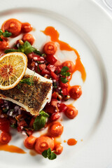 Black cod fillet on a vegetable stew, festive serving on a white grater on a table with white tablecloths.