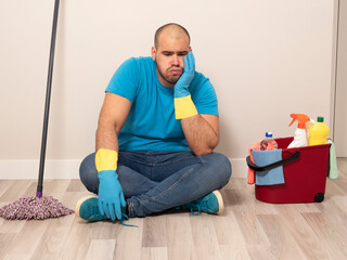 Young man cleaning with a sweeping brush and mop and bucket of water and cleaning supplies at home...