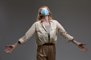A woman in a mask and glasses makes a helpless gesture of hopelessness, covid 19 concept, gray...