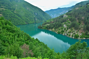Fototapeta na wymiar The turquoise waters of Koman Lake surrounded by green cliffs