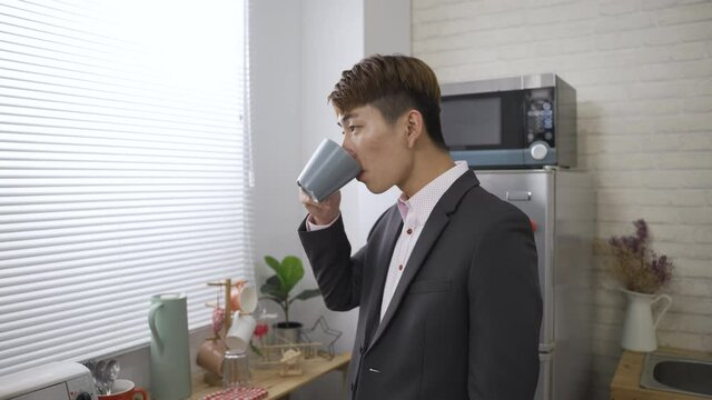 Japanese business man is exercising neck muscles while looking outside the window and enjoying morning tea at leisure in a cozy home interior with daylight.