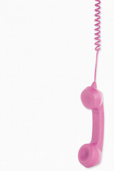 retro pink telephone receiver dangling from telephone cord on white background