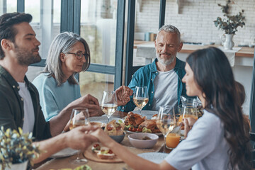 Happy multi-generation family holding hands and praying before having dinner