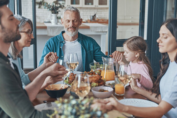 Happy multi-generation family holding hands and praying before having dinner