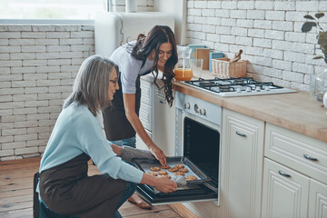 Beautiful young woman and her mother cooking together while spending time at the domestic kitchen