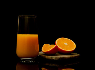Orange juice in a glass with fruit slice hovering on the dark black background