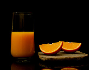 Orange juice in a glass with fruit slice hovering on the dark black background