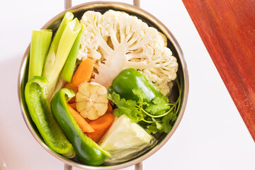 Various fresh vegetables in a pot; colorful fresh clear spring soup (vegetarian stock) cauliflower, broccoli, carrots, garlic, bell pepper and onion.