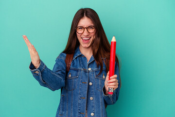 Young student caucasian woman holding a big pencil isolated on blue background receiving a pleasant...