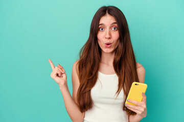 Young caucasian woman holding a mobile phone isolated on blue background pointing to the side