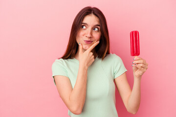 Young caucasian woman holding an ice cream isolated on blue background looking sideways with doubtful and skeptical expression.