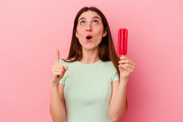 Young caucasian woman holding an ice cream isolated on blue background pointing upside with opened mouth.