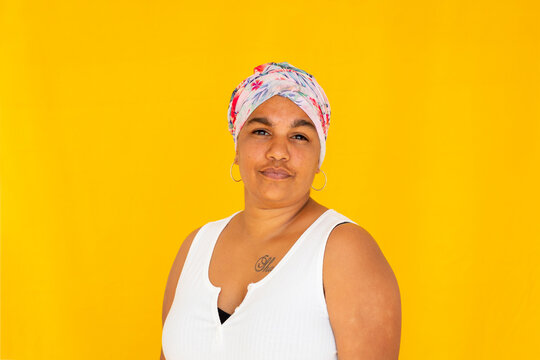 Head and shoulders of Indigenous woman wearing floral head wrap against bright yellow background