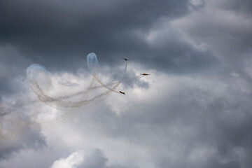 a group of combat aircraft perform complex aerobatics with a smoke launch against the sky
