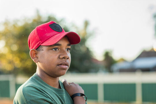 head and shoulders of adolescent wearing red baseball cap looking off into distance