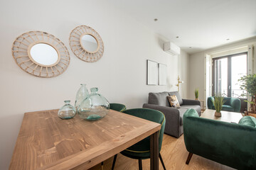 Office table for meals decorated with glass containers and circular mirrors on the wall in a vacation rental apartment with green velvet sofas and chairs