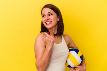 Young caucasian woman playing volleyball isolated on yellow background points with thumb finger away, laughing and carefree.