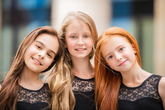 Portrait of three teenage girls with loose hair, blonde, redhead and brunette Summer on street. Vloses develop in wind.