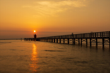 Paesaggio di mare. Alba al vecchio faro rosso di Lignano con pensilina, banchina in legno.