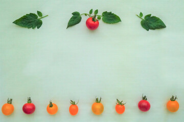 ペールグリーンのクロスを背景に上下に並んだ赤と黄のミニトマトと葉の飾り枠