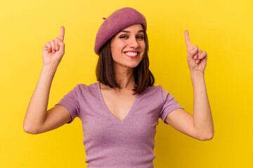 Young caucasian woman isolated on yellow background indicates with both fore fingers up showing a...