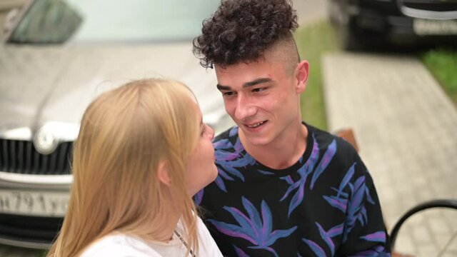 A stylish young man smiles at his girlfriend, with whom he sits on a bench and communicates. Meeting of two young people in the city, date of a couple. Slow motion