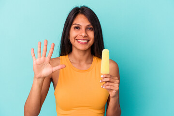 Young latin woman holding ice cream isolated on blue background smiling cheerful showing number five with fingers.