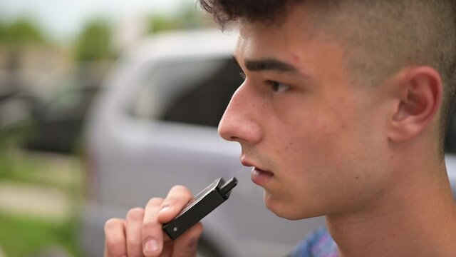 Young cute guy smoking an electronic cigarette in the city, close-up, slow motion