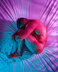 Naked man in fetal position in multicolored light