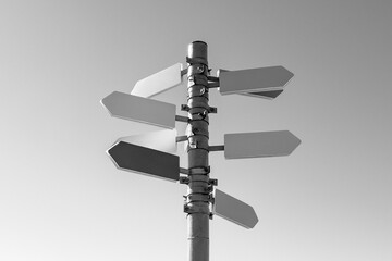 Guidepost with arrows in sunlight against sky background. Black and white photography.