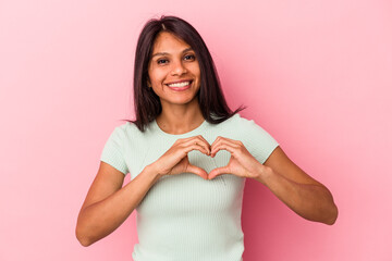 Young latin woman isolated on pink background smiling and showing a heart shape with hands.