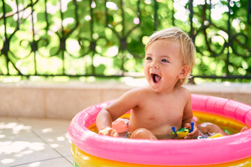 Laughing baby sits in a small inflatable pool with toys
