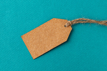 Blank cardboard tag on a flax twine over turquoise background. Brown paper tag with jute rope against textured teal surface. Recyclable rope tag of natural materials. Copy space.